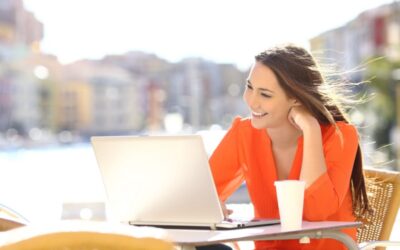 woman sitting outside at a table with a laptop smiling