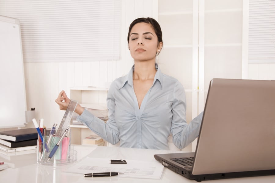 woman meditating at desk with laptop