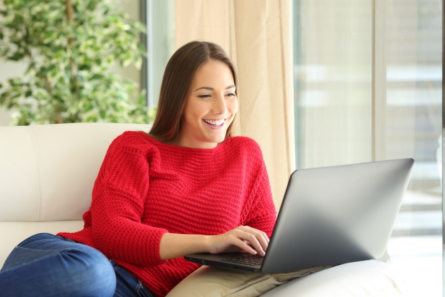 woman in red sweater sitting on couch working on her laptop