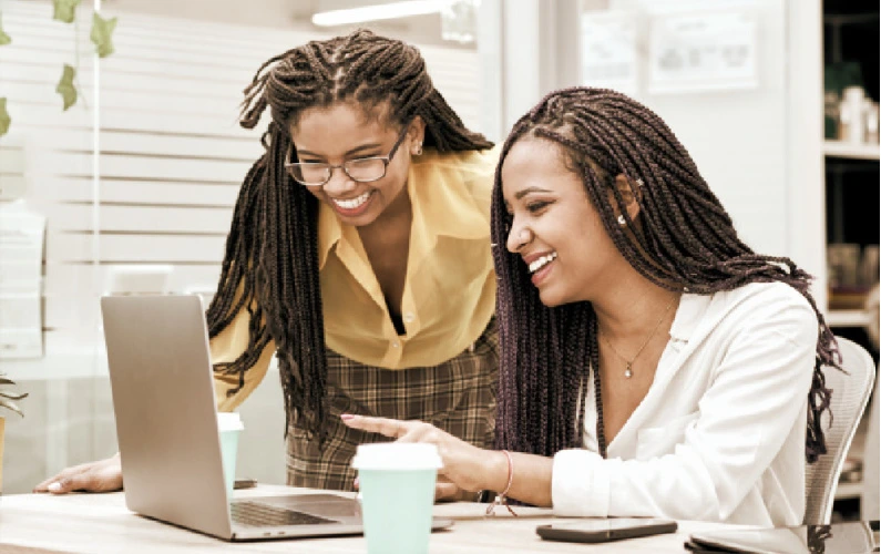 two women smiling looking at their website on a laptop