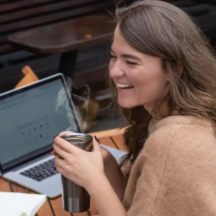 Happy woman sitting with coffee working on laptop