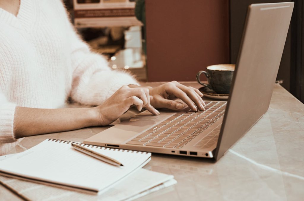 woman wellness coach with notepad typing on laptop